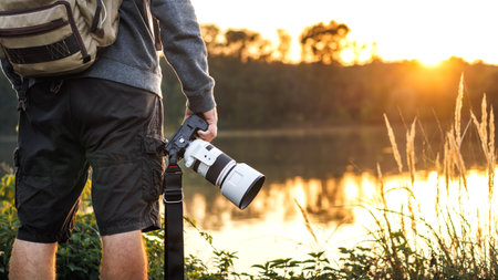 Landscape and wildlife photographer holding camera with telephoto lens and looking for composition at lake during sunsetの写真素材