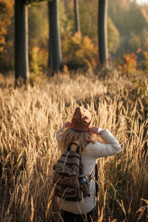 Woman with backpack, jacket and knit hat walks in golden grass. Autumn hiking in forest. Outdoor warm clothingの写真素材