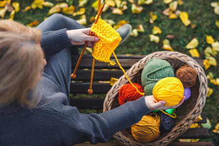 Knitting warm clothing from yarn. Woman choosing yellow ball of wool from basket. Relax on bench in autumn parkの写真素材