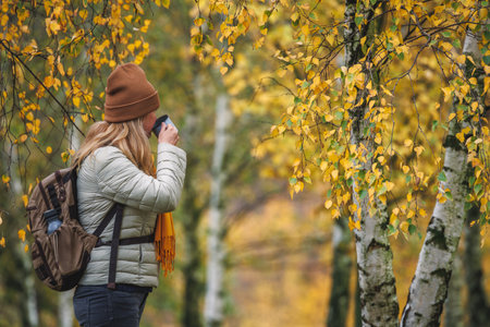 Woman drinking hot tea from travel mug during hike in autumn forest. Enjoying woodland in fall seasonの写真素材