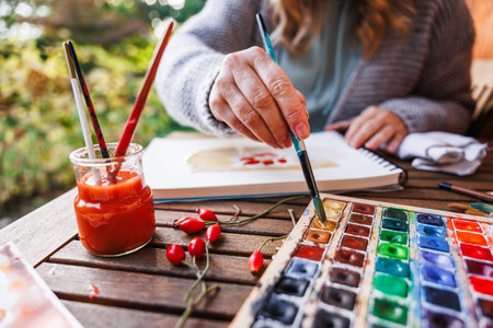 Woman artist dips paintbrush into color palette and paints a watercolor illustrationの写真素材