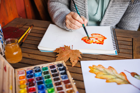 Watercolor painting. Woman artist paints an autumn theme on paper. Palette of colors on the table