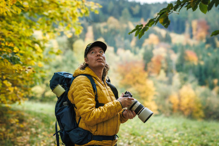 Man with camera and backpack hiking in autumn forest. Bird watching and nature exploringの写真素材