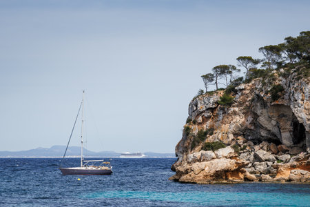 Anchored yacht in the bay of Portals Vells in Mallorca. Cruise ship in the distance sails in the Mediterranean Sea. Holiday destination in the Balearic Islandsの写真素材