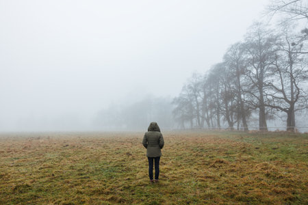 Solitude female person in the fog. Lonely woman in hooded coat standing in foggy nature. Loneliness conceptの写真素材