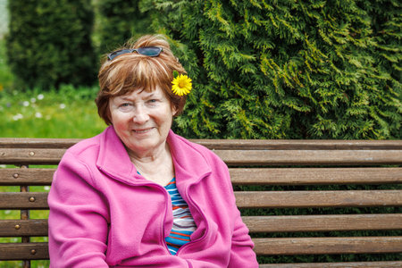 Portrait of happy smiling senior woman is relaxing on bench in garden at springtime. Enjoyment of beautiful spring dayの写真素材