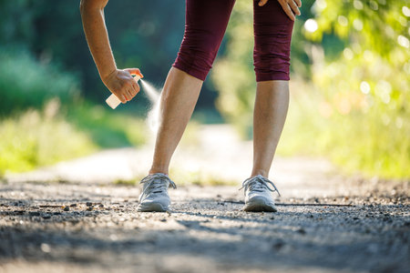 Woman spraying insect repellent against mosquito and tick on her leg before jogging in natureの写真素材