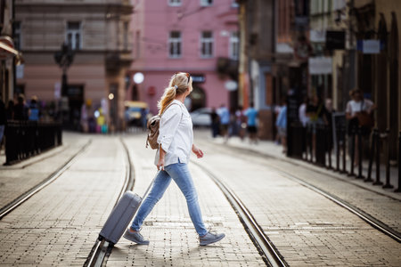 Woman tourist with suitcase walks across city street. Secure journey with reliable travel insuranceの写真素材
