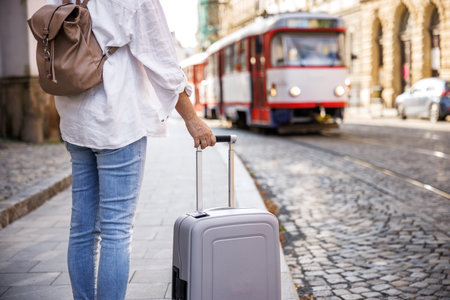 Woman tourist with suitcase and backpack waiting for tram on street. Travel by public transportation in the cityの写真素材