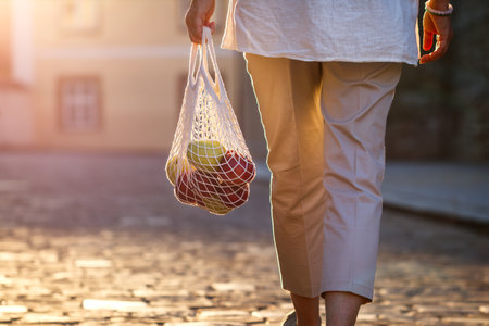 Woman walks on street and carrying reusable mesh bag with apple fruits. Plastic free and zero waste sustainable shopping lifestyleの写真素材
