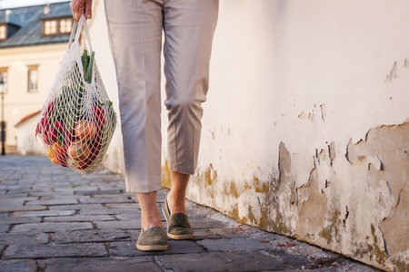 Woman walks on street with reusable mesh bag after shopping food. Zero waste and sustainable plastic free lifestyleの写真素材