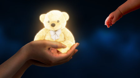 Glowing teddy bear in the hands of a women giving to a baby on a dark backgroundの写真素材