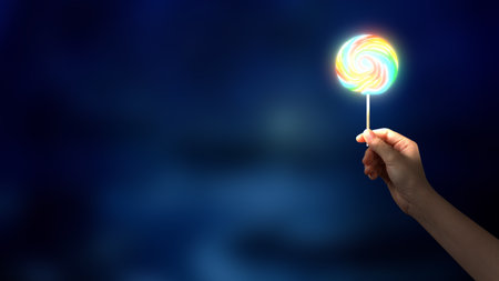 Close up of woman hand holding colorful lollipop on dark backgroundの写真素材