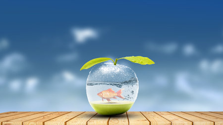 Goldfish in a glass apple concept on a wooden table against the skyの写真素材