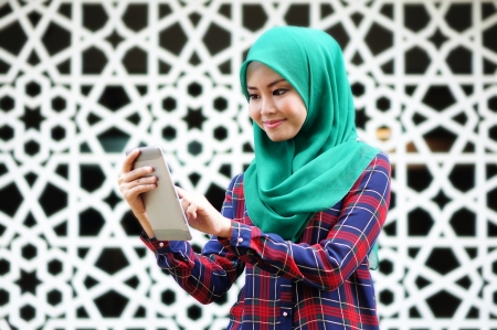 young muslim woman using tablet phone in front of islamic backgroundの写真素材