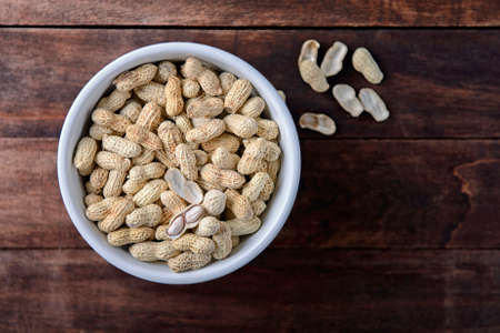 Peanuts in white bowl on wooden backgound