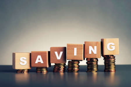 saving text written on wooden block with stacked coins on grey background