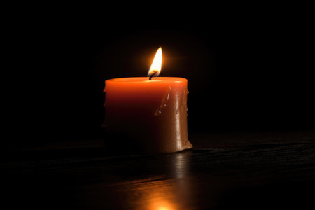 A single, lit candle stands against a dark, minimalist background, representing the simple warmth and light it provides. The image evokes a sense of peace, tranquility, and meditation.の素材