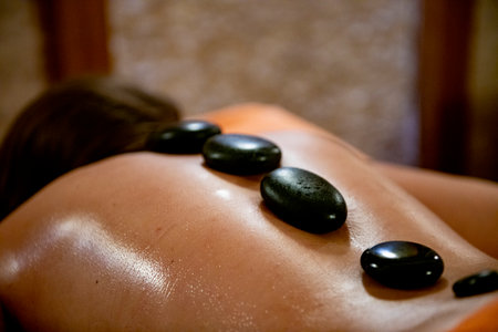 Spa massage with hot stones on the back of a young womanの写真素材