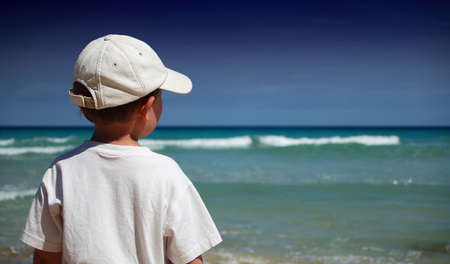Boy in white shirt watches the waves on the beachの写真素材