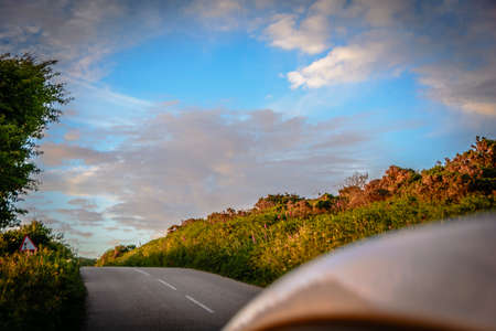 Sun rays through the forest and car on the street in cornwall england in summerの写真素材