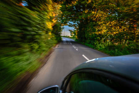 Sun rays through the forest and car on the street in cornwall england in summerの写真素材