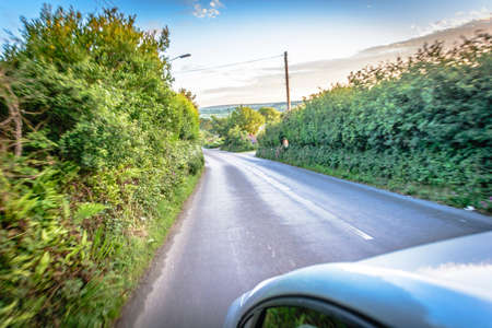 Sun rays through the forest and car on the street in cornwall england in summerの写真素材