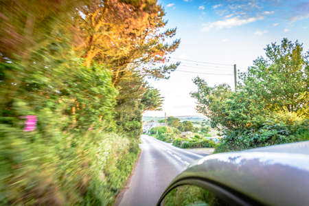 Sun rays through the forest and car on the street in cornwall england in summer