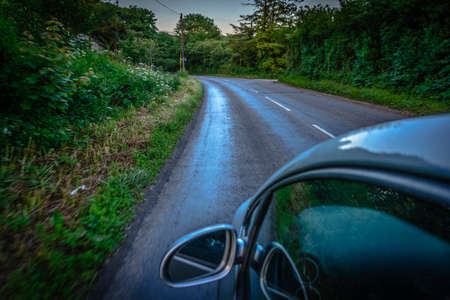 Sun rays through the forest and car on the street in cornwall england in summerの写真素材