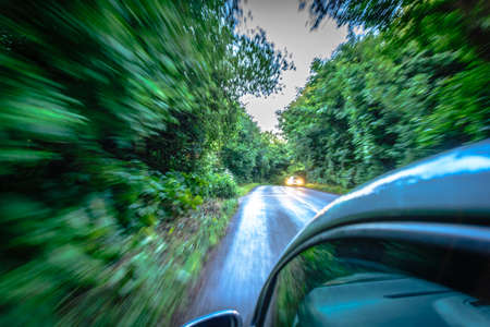 Sun rays through the forest and car on the street in cornwall england in summerの写真素材