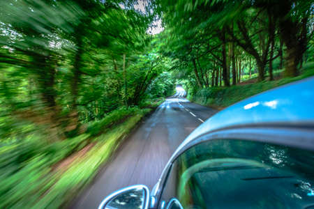 Sun rays through the forest and car on the street in cornwall england in summerの写真素材