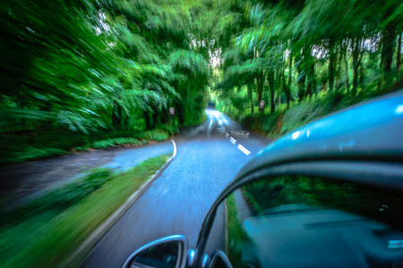Sun rays through the forest and car on the street in cornwall england in summerの写真素材