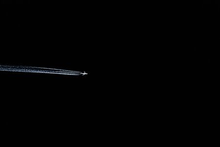 airplane flies in a dark sky leaving behind a large trailの写真素材