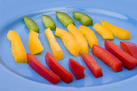 sliced yellow, green and red pepper on blue plateの写真素材