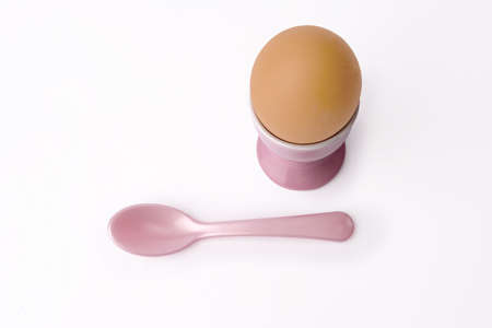 brown egg in egg cup with spoon on white backgroundの写真素材