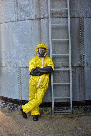 specialist in protective uniform standing at the front of  metal ladder of large industrial  silo