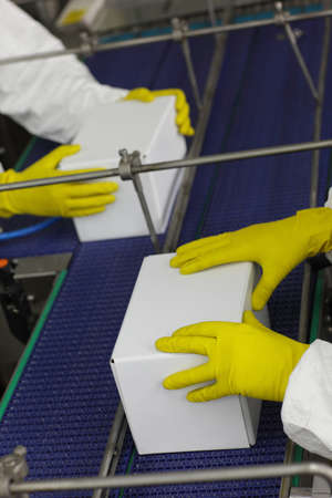 Workers in protective uniforms and gloves working with  boxes  at automatic production line in factoryの写真素材