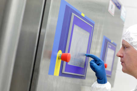 technician in white cap and blue gloves touching screen at control panel in plant