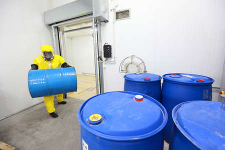 Worker in protective uniform,mask,gloves and boots carrying barrel of chemicals の写真素材