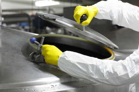 hands in yellow gloves opening industrial process tank - close up 