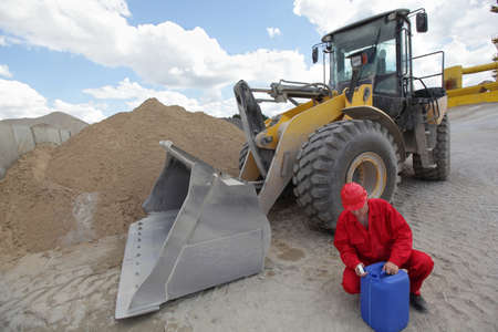 operator in red uniform checking petrol can, large bulldozer in backgroundの写真素材