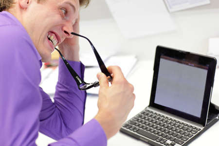 stressed business man biting rims of eye glasses looking at screen of table in office