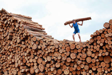 man on top of large pile of logs, lifting heavy log - training
