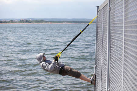 hooded man outdoor,suspension training at the sea の写真素材