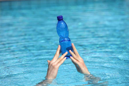 two hands raising out of water holding plastic blue bottle of water 