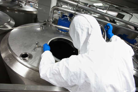 Specialist in protective uniform,mask,goggles,gloves controlling industrial process,back viewの写真素材