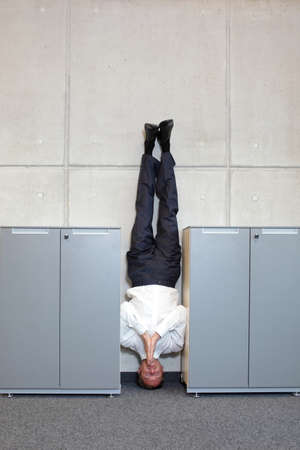 business man standing on his head between cabinets in officeの写真素材