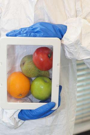 Scientist dressed in protective gear holding fruits and vegetables in plastic container - close up