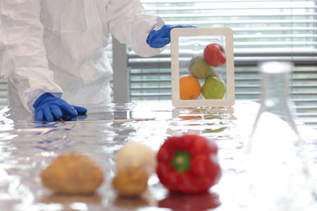 Scientist dressed in protective gear holding fruits and vegetables in plastic container