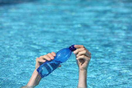 two hands holding plastic bottle of water  above surface of water